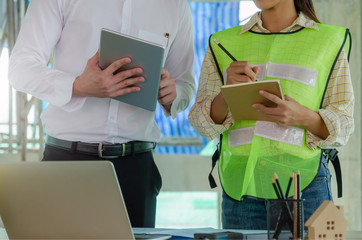 construction worker team writing and planning about building plan with mobile tablet, laptop, construction tools on conference table at construction site, contractor, industry and construction concept
