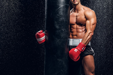 Beautiful muscular fighter with naked torso is standing at dark room with water drops on the wall.