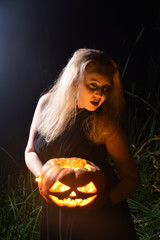 Witch holding a Jack pumpkin in her hands. Halloween party concept. Beautiful young woman plays the role of a witch on a holiday.
