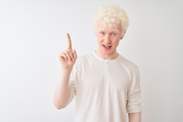 Young albino blond man wearing casual t-shirt standing over isolated white background pointing finger up with successful idea. Exited and happy. Number one.