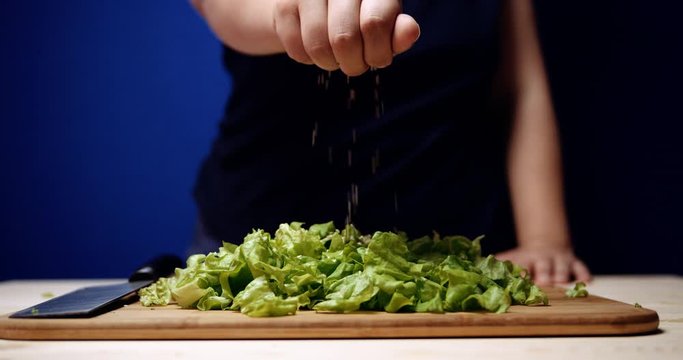 girl sprinkles sesame seeds on sliced lettuce lying on a wooden cutting board