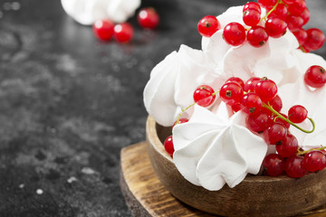 White meringue with currants in a wooden bowl on a black table. French dessert. Place for text