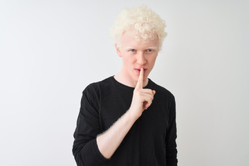 Young albino blond man wearing black t-shirt standing over isolated white background asking to be quiet with finger on lips. Silence and secret concept.