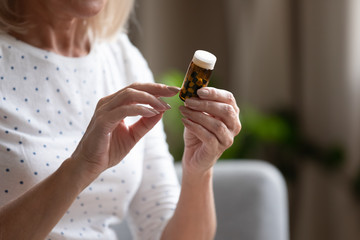 Close up mature woman holding bottle with pills, reading instruction