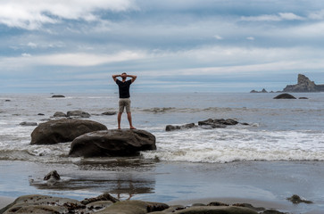 Man standing on rock with arms resting on the back of his neck taking in ocean sky view