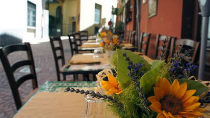 eine bunte Strasse in Italien im Sommer mit Tischen von einem Restaurant und Blumen auf dem Tisch