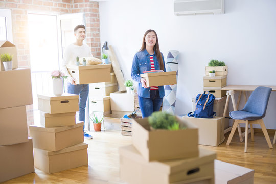 Beautiful young asian couple looking happy holding cardboard boxes, smiling excited moving to a new home