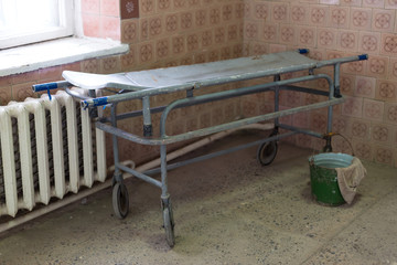 Old stretcher gurney bed in the hospital hallway. Bucket and rag. A horrible old hospital or morgue.