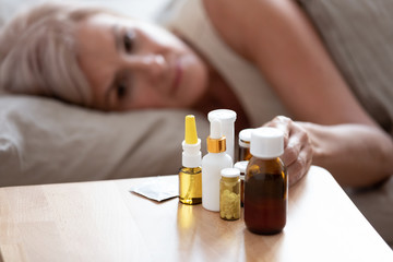 Unhealthy mature woman lying in bed, taking pills close up
