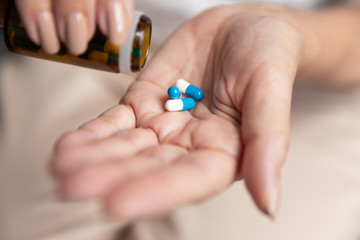 Mature woman taking out dose of pills from glass bottle