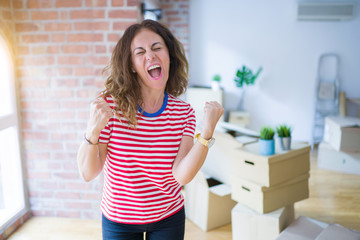 Middle age senior woman moving to a new house packing cardboard boxes very happy and excited doing...