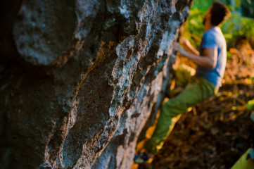 extreme lifestyle of young active sport man climbing on outdoor rock during bouldering training on warm sunset in forest