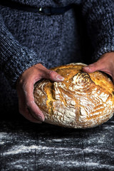 hands holding appetizing round bread with white powder on a dark background