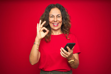 Naklejka premium Middle age senior woman using smartphone over red isolated background doing ok sign with fingers, excellent symbol