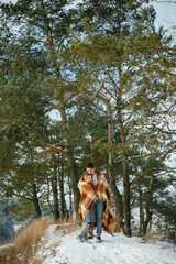 Fototapeta premium happy couple wrapped in a blanket standing in the park on a snowy day