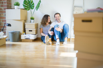 Middle age senior romantic couple in love sitting on the apartment floor with cardboard boxes around and smiling happy for moving to a new home