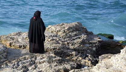 Muslima in schwarzer Abaya an der felsigen Levanteküste