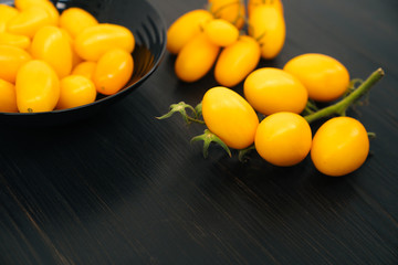 Top view, yellow cherry tomatoes in bowl on black wooden background, copy space