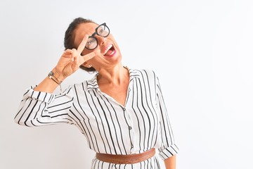 Middle age businesswoman wearing striped dress and glasses over isolated white background Doing peace symbol with fingers over face, smiling cheerful showing victory