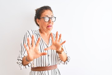 Middle age businesswoman wearing striped dress and glasses over isolated white background afraid...