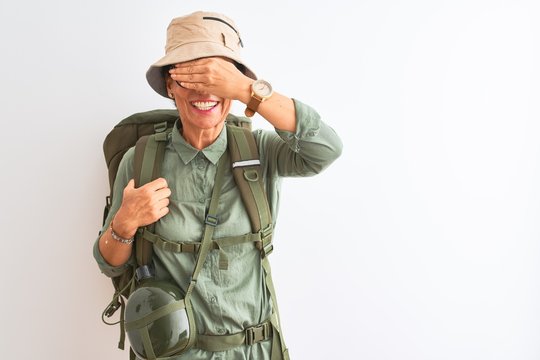 Middle age hiker woman wearing backpack canteen hat glasses over isolated white background smiling and laughing with hand on face covering eyes for surprise. Blind concept. - Powered by Adobe