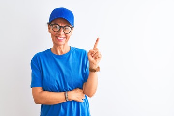 Senior deliverywoman wearing cap and glasses standing over isolated white background with a big smile on face, pointing with hand and finger to the side looking at the camera.