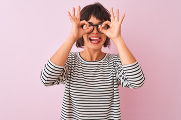 Young beautiful woman wearing striped t-shirt and glasses over isolated pink background doing ok gesture like binoculars sticking tongue out, eyes looking through fingers. Crazy expression.