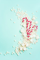 Naklejka premium Christmas or New year holiday layout with candy canes and marshmallows on a turquoise background with copy space. Greeting card with Christmas props.