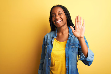 Young african american woman wearing denim shirt standing over isolated yellow background Waiving...