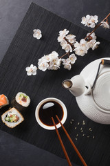 Set of sushi and maki rolls with branch of white flowers and teapot with the inscription green tea on stone table