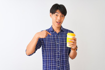 Young chinese man drinking take away coffee standing over isolated white background with surprise face pointing finger to himself