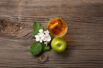 Ripe green apples with branch of white flowers and glass of fresh juice on a wooden table