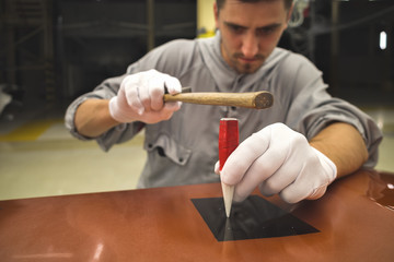 Employee of the dealership on painting the body learns to repair small defects in the metal