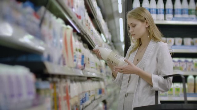 Advertise, Business, Food, Health Concept - Woman in a supermarket standing in front of the freezer and choose buying fresh milk bottle. Drink milk for healthy