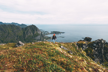 Traveler man wearing backpack and red hat climb on high mountains above sea. Professional expeditor standing on the edge cliff rock and looking forward away. Wanderlust