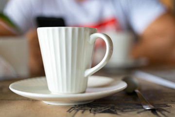 one ceramic cup of coffee in the foreground on a blurred background of the second cup and a man with a phone in his hand