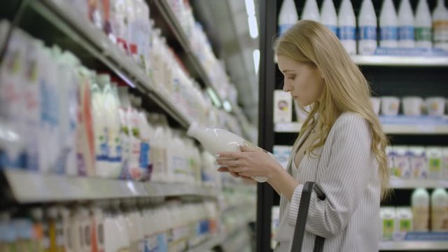 Advertise, Business, Food, Health Concept - Woman in a supermarket standing in front of the freezer and choose buying fresh milk bottle. Drink milk for healthy