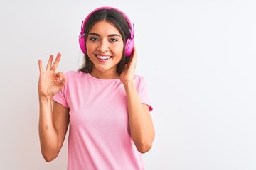 Obraz na płótnie Canvas Young beautiful woman listening to music using headphones over isolated white background doing ok sign with fingers, excellent symbol
