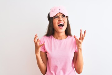 Young beautiful woman wearing sleep mask standing over isolated white background crazy and mad...