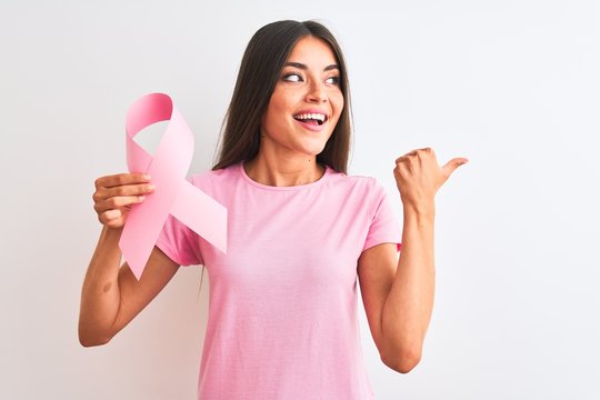 Young beautiful woman holding cancer ribbon standing over isolated white background pointing and showing with thumb up to the side with happy face smiling