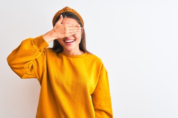 Young beautiful woman wearing yellow sweater and diadem over isolated white background smiling and laughing with hand on face covering eyes for surprise. Blind concept.