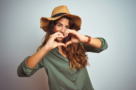 Young beautiful woman on vacation wearing green shirt and hat over white isolated background smiling in love showing heart symbol and shape with hands. Romantic concept.