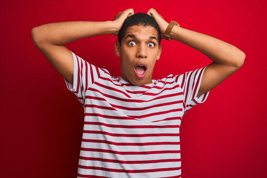 Young handsome arab man wearing striped t-shirt over isolated red background Crazy and scared with hands on head, afraid and surprised of shock with open mouth