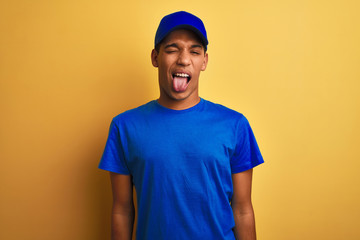 Young handsome arab delivery man standing over isolated yellow background sticking tongue out happy with funny expression. Emotion concept.