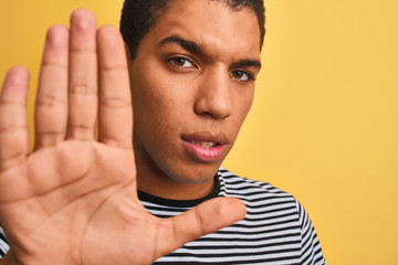 Young handsome arab man wearing navy striped t-shirt over isolated yellow background with open hand doing stop sign with serious and confident expression, defense gesture