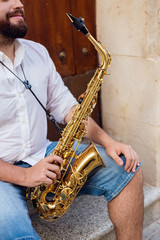 Naklejka premium Close up of a man sitting at the door of a building on the street holding his saxophone