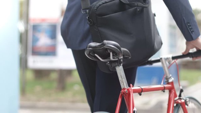 Amazing tracking shot portrait of handsome young businessman with a briefcase on the shoulder and a bike helmet pushing his bike in the city at sunrise or sunset.