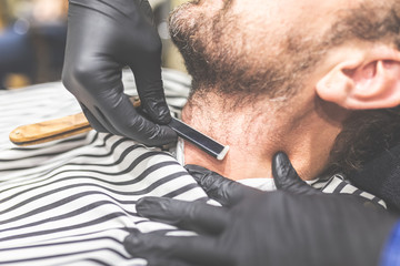 Making hair look magical. Close-up side view of young bearded man getting shaved with straight edge...