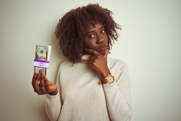 Young african afro woman holding dollars standing over isolated white background serious face...