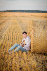 young guy is relaxing in the countryside with a guitar. Plays the guitar . Resting lying on the hay